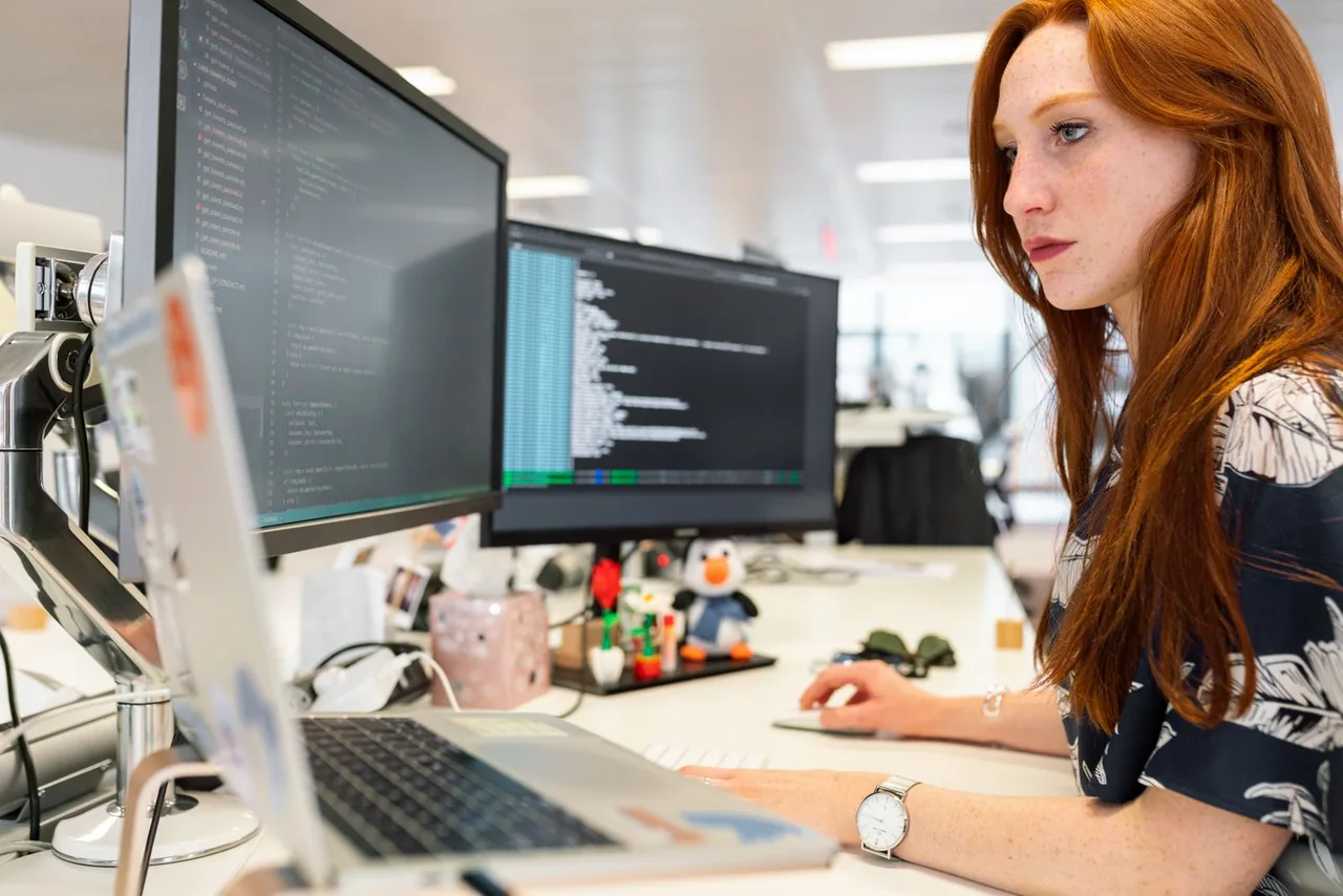 Eine Softwareentwicklerin arbeitet konzentriert am Code an zwei Bildschirmen.