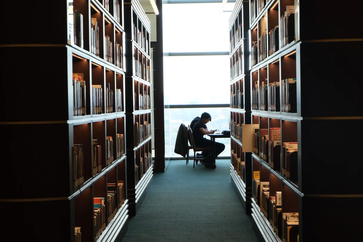 A reader between tall library bookshelves.